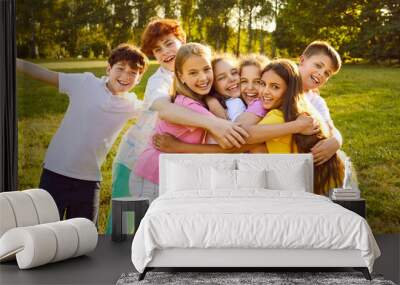 Children have fun and make friends at the summer camp. Group of kids spending time outdoors together. Bunch of happy girls and boys hugging each other in a green sunny park Wall mural