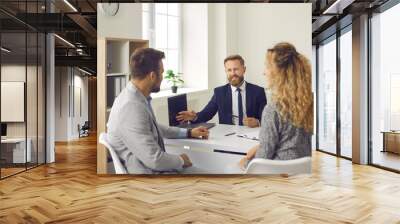 Clients talking to bank manager. Young married couple meeting with realtor, real estate agent or mortgage advisor. Man and woman sitting at office desk and having discussion with insurance broker Wall mural