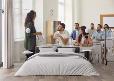 College teacher having class with group of interested adult male and female business course students. People sitting at tables in classroom, discussing topic of success, asking or answering questions Wall mural