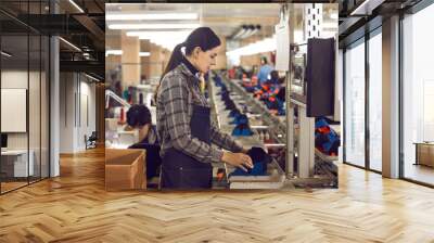 Concentrated young female manufacturing workshop worker making shoe at mass production line of footwear factory. Woman shoemaker using machine equipment. Profession and industry concept Wall mural