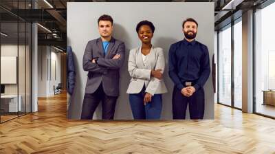 Confident business team in modern smart clothes. Group of happy young diverse people in formal suits standing in fashion studio and leaning on gray wall. Office dress code concept. Banner, header Wall mural