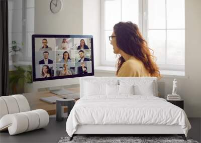 Corporate business team having a remote meeting. Young woman in casual clothes sitting at her desk at home, attending an online conference, looking at the computer screen, and smiling Wall mural