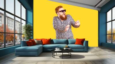 Crazy plus size man in funny pajamas dancing and having fun in fashion studio. Happy bearded fat guy wearing cool sunglasses and comfy leopard PJs singing and dancing isolated on yellow background Wall mural