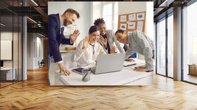 Creative business team having online video conference meeting with international partners. Group of happy mixed race people smiling and waving hands at laptop computer saying hello to their coworkers Wall mural