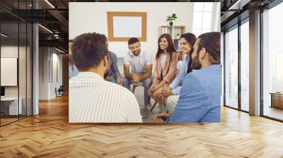 Different people sitting in a circle, talking and smiling during a group therapy session. Team of happy cheerful positive young and mature men and women having a meeting Wall mural