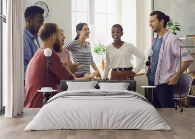 Diverse group of happy cheerful friends meet and have fun together. Bunch of positive young multiracial people standing in office or living-room, talking, sharing news and funny stories and laughing Wall mural