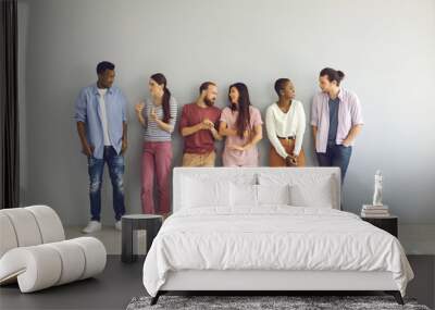 Diverse people leaning on studio background and talking. Full body length indoor group shot of happy young men and women making friends, sharing and listening to opinions and finding common grounds Wall mural