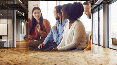 Diverse people sitting on row of chairs and talking. Group of happy young and mature black and white male and female meeting members sharing opinion and making suggestions for changes and improvements Wall mural