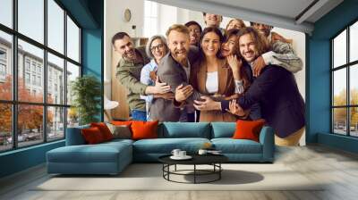 Diverse team of happy business people. Group portrait joyful young and senior Caucasian and African American men and women friends coworkers standing in office, hugging, looking at camera and smiling Wall mural