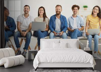 DIverse team of happy modern corporate company workers having fun at work. Group of joyful mixed race multiethnic people in T shirts and jeans with laptops and notebooks sitting in office and laughing Wall mural