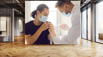 Doctor medical worker in uniform and face mask making injection of vaccination for protection from 19-ncov infection for asian man patient. Vaccinating against COVID-19 infection during pandemic Wall mural