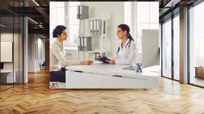 Doctor woman pediatrician gynecologist talking client sitting at a table in a clinic office. Wall mural