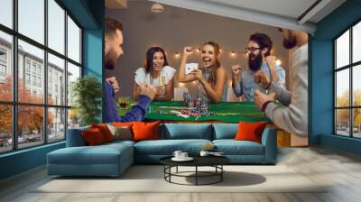 Excited woman showing 2 aces sitting at poker table with happy friends at casino themed party Wall mural