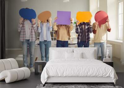 Faceless people sharing message or expressing opinion in anonymous survey. Group of unrecognizable young college or university students covering faces with multicolored paper mockup speech bubbles Wall mural