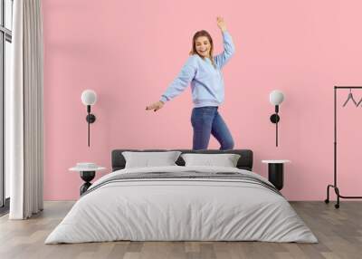 Female model having fun in the fashion studio. Cheerful young girl dancing and laughing. Full body shot of a pretty woman in comfortable casual outfit dancing isolated on pastel pink colour background Wall mural