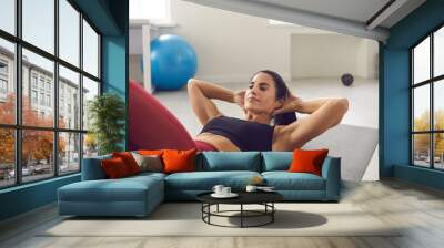 Fit woman exercising her abs by doing crunches or sit-ups lying on sports mat on the floor during routine fitness workout at home. Concept of regular training and reaching perfect body Wall mural