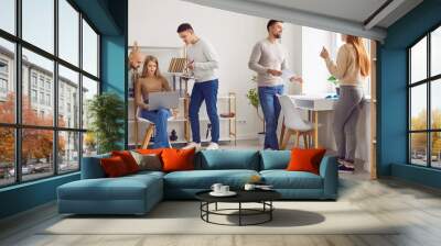 Friendly atmosphere in team. Portrait of company staff working and talking in modern office during working day. Young Caucasian men and women in casual clothes working amicably in coworking space. Wall mural