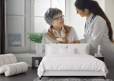 Friendly female nurse teaches an older woman to use modern health programs on her mobile phone. Caring doctor talks to an elderly patient. Concept of medicine and modern technology. Wall mural