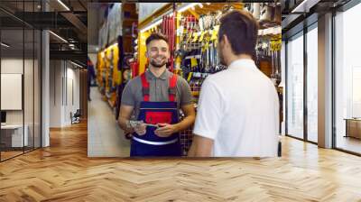 Friendly shop assistant at DIY retail store helping customer choose tools and equipment. Happy smiling salesman helping young man who is buying wrenches and other tools for home repairs Wall mural