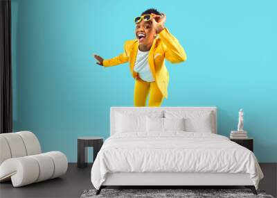 Full body shot happy cheerful confident young Afro American woman wearing stylish bright yellow suit and sunglasses standing isolated on blue background, looking at camera and smiling. Fashion concept Wall mural