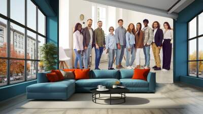 Full length portrait of young happy group of business multiethnic people men and women looking at camera and smiling indoors. Company employees or group of staff standing in office. Wall mural