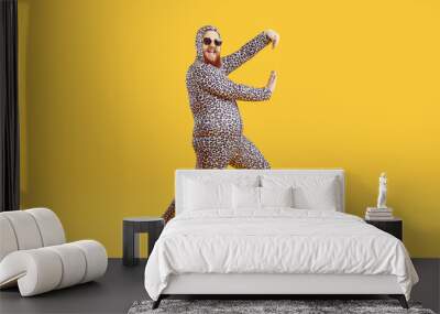 Funny chubby guy in crazy costume having fun in modern fashion studio. Happy cheerful confident fat man wearing comfortable leopard pajamas dancing isolated on yellow background. Crazy party concept Wall mural