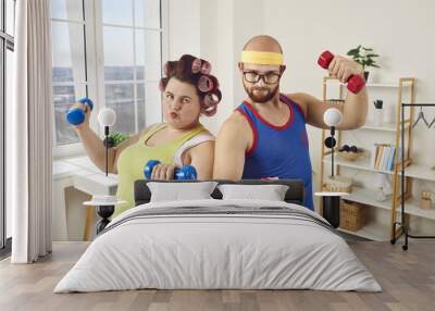 Funny couple of fat woman and unshaven man exercising with dumbbells at home. Ridiculous plus size woman and man in bright sportswear doing fitness exercises together. Healthy lifestyle, weight loss Wall mural