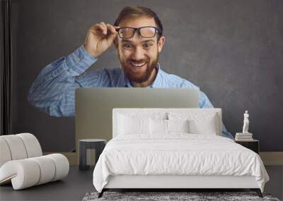 Funny excited surprised man takes off glasses looking at screen of laptop computer device. Happy lucky guy gets job offer business email, wins a cool prize or earns easy money on gaming website Wall mural