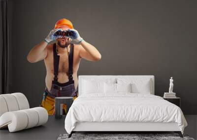 Funny fat bearded repairman with binoculars on a gray background. Wall mural