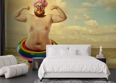 Funny man in a swimsuit with an inflatable circle on the beach Wall mural