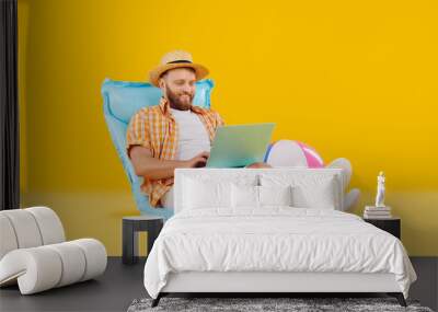 Funny man in casual summer clothes relaxing sitting on inflatable mattress working or booking tickets online isolated on a yellow background. Summer vacation, holiday trip or remote work concept Wall mural