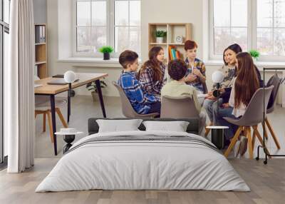 Group of elementary school children and their teacher discussing something while sitting in a circle on comfortable chairs in a modern classroom all together Wall mural