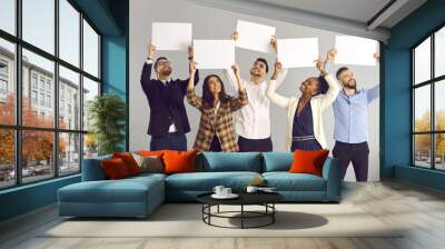 Group of five happy smiling people, office workers or friends, standing on gray background, holding white sheets of paper, empty signs, mockup banners, expressing opinion or giving positive feedback Wall mural