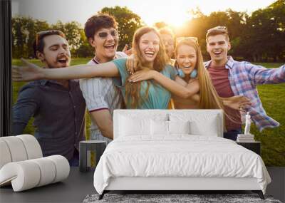 Group of happy and carefree young friends who are laughing in summer park with open arms to camera. Funny joyful young people having fun together outdoors on summer sunny day. Friendship concept. Wall mural