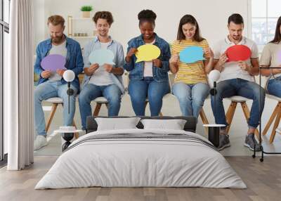 Group of happy diverse mixed race people taking part in public opinion survey, sitting in row in new modern office and looking at colorful mockup text speech balloons they are holding in hands Wall mural