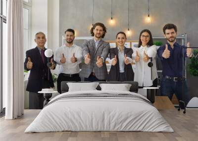 Group of happy male and female company workers giving thumbs up standing by office table after successful business meeting. Working in dream team, achieving success, teamwork, job satisfaction concept Wall mural