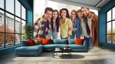 Group of happy smiling funny friends students or colleagues in casual clothes standing together and looking cheerful and positively at the camera. Portrait of friendly guys and girls indoors. Wall mural