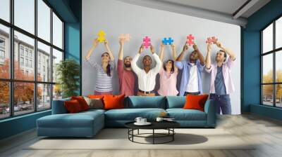 Group of happy smiling multiracial young people holding colorful puzzle pieces over their heads. Creative people stand on a light wall background. Concept of teamwork and cooperation. Wall mural