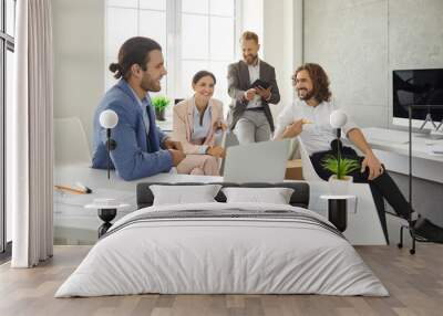 Group of happy young business people having a meeting in a modern office. Team of positive smiling corporate employees working on a project together, using a laptop computer, talking and sharing ideas Wall mural