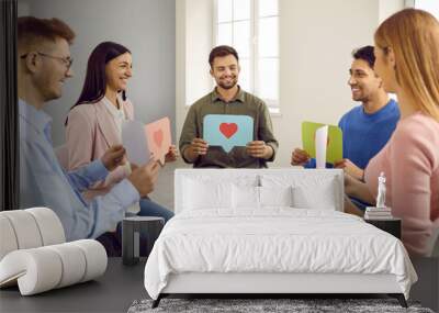 Group of happy young people sitting in circle, smiling and showing paper chat message bubbles with heart symbols. Communication, support, positive feedback, friendship, love, online dating concepts Wall mural