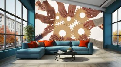 Group of multiracial people joining gear wheels together as metaphor for effective team collaboration, unity, teamwork, finding working solutions and creating business systems. From below, low angle Wall mural