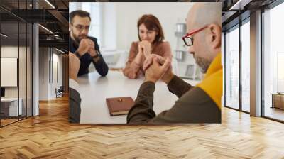 Group of people praying together. Different men and women sitting around the table with the Holy Bible and cross and saying a prayer, thanking God for his grace and forgiveness Wall mural