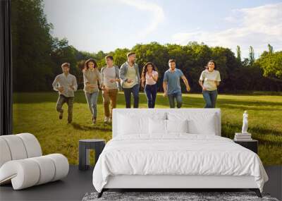 Group of several happy, cheerful friends having fun on a sunny summer day in nature. Seven happy young people running together on a green grass lawn in the park Wall mural