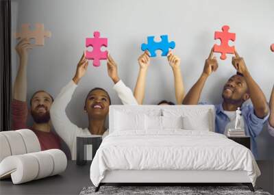 Group of six happy smiling young people holding big colorful jigsaw puzzle pieces standing against light grey studio background. Team of creative millennials cooperate and find good solution together Wall mural