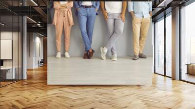 Group of successful confident business people in smart and casual wear standing in studio. Team of employees leaning on grey office wall. Cropped shot of people's legs in classic pants and jeans Wall mural