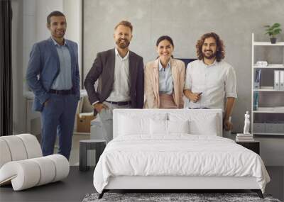 Group portrait of four happy confident young business people at work. Team of 4 corporate employees and yuppies in smart stylish suits standing in office all together, looking at camera and smiling Wall mural