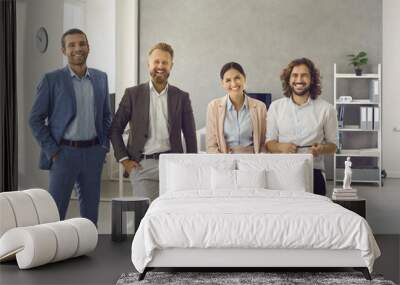 Group portrait of four happy positive young business professionals at work. Team of 4 cheerful confident people in smart suits standing in office all together, looking at camera and smiling Wall mural