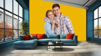 Happy beautiful romantic teenage couple. Older brother and sister with toothy smiles. Handsome Caucasian man and young woman in shirts standing in studio, hugging each other, sharing positive emotions Wall mural