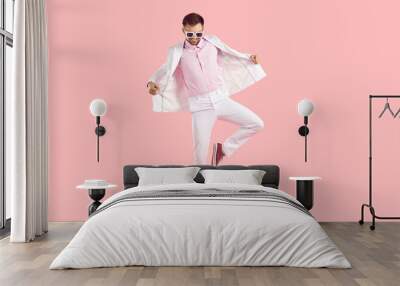 Happy carefree man having fun in the studio. Funny attractive young guy wearing white suit, pink shirt, modern sunglasses and comfortable trainer shoes dancing isolated on solid pink color background Wall mural