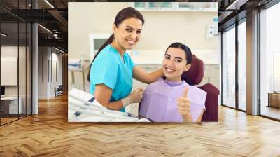 Happy client in dentist's office recommending dental clinic satisfied with good service provided by hygienist. Smiling female patient giving thumbs up and looking at camera during regular checkup Wall mural